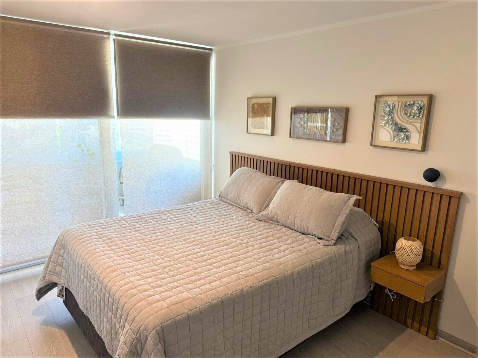 A bedroom with a bed, a nightstand, a lamp, and three framed pictures on the wall.
