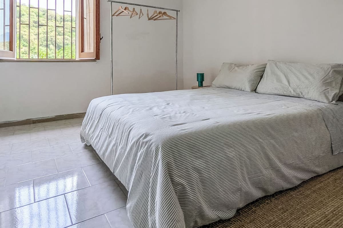 A bedroom with a bed, a window, a hanging light fixture, and a wardrobe.