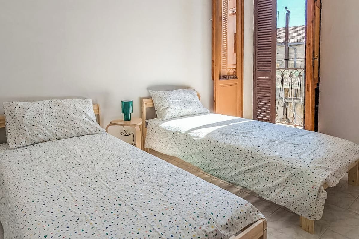 A bedroom with two wooden beds, a nightstand, and a window with wooden shutters.