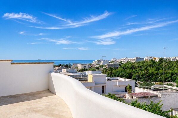 A rooftop terrace with a view of a coastal town, buildings, and greenery.