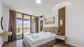 A hotel room with a large bed, a view through a sliding door, a painting on the wall, and a wooden floor. - Adriatic Escape Apartment | Steps from the Beach by PikHost (Lezha)