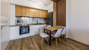 A compact kitchen with wooden cabinets, a built-in oven, a dining table with chairs, and a modern pendant light. - Adriatic Escape Apartment | Steps from the Beach by PikHost (Lezha)