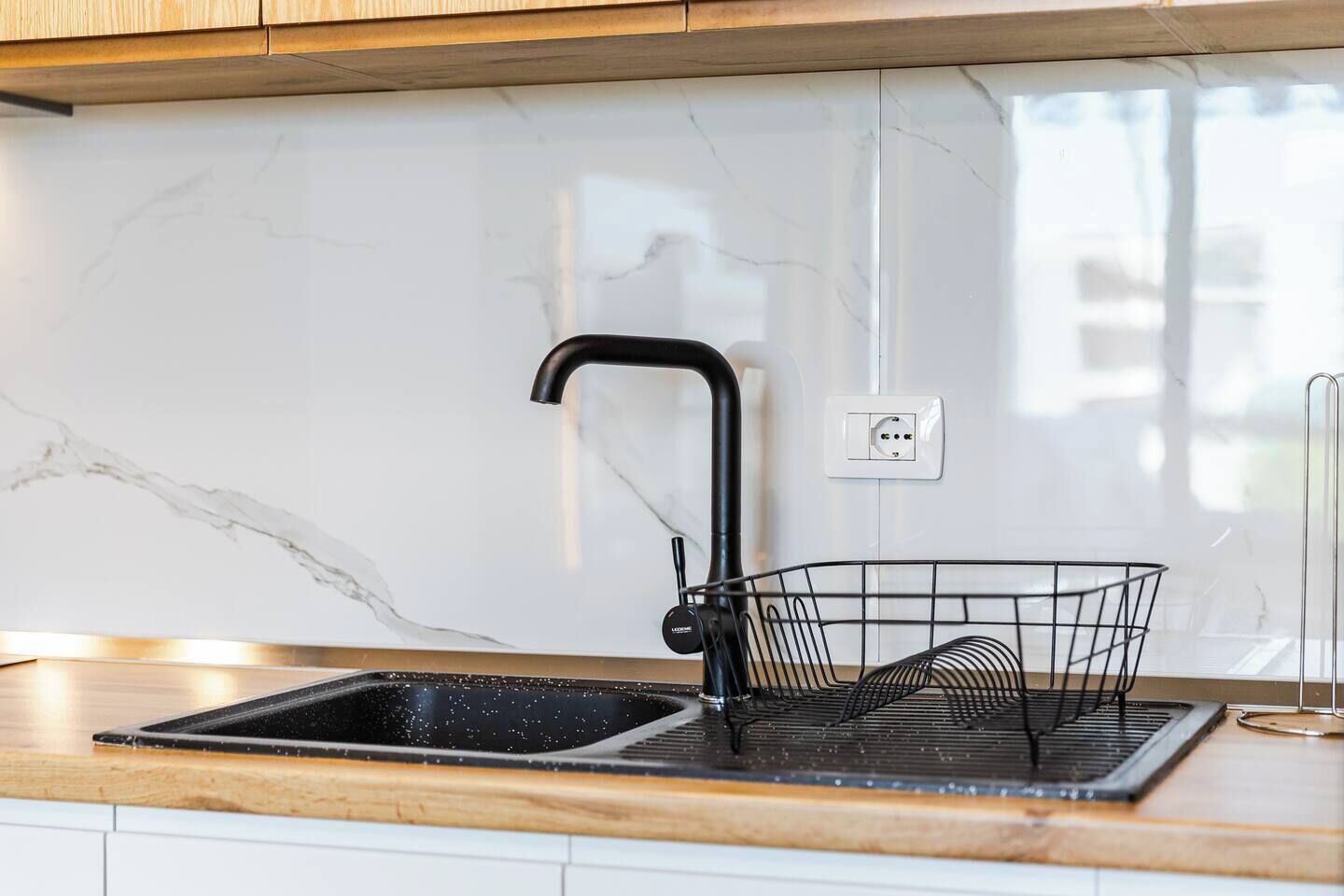 A kitchen with a black faucet, a sink, a wire basket, and a marble backsplash.