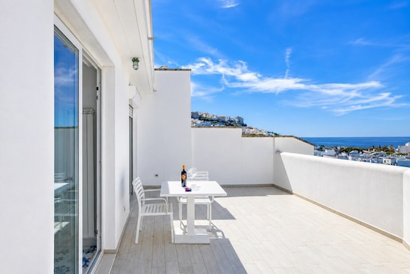 A white balcony with a table and chairs, a bottle of wine, and a glass.