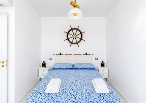A bedroom with a bed, two bedside tables, a wall-mounted ship's wheel, and a ceiling light fixture.