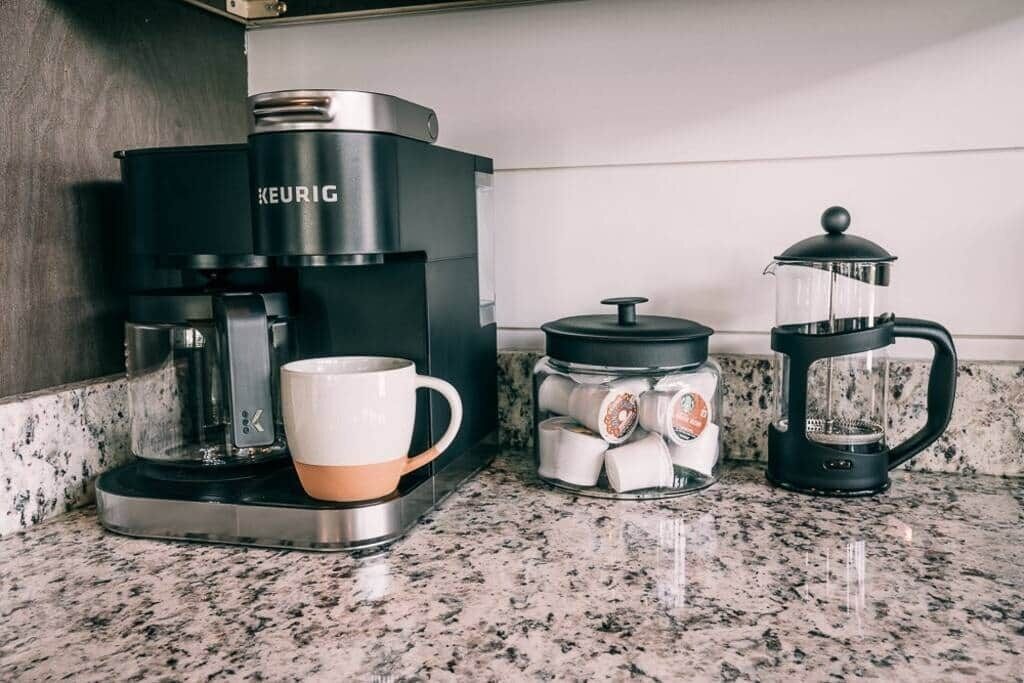 Kaffemaskine, stempelkande og en kop på en køkkenbordplade.