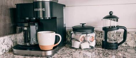 Kaffemaskine, stempelkande og en kop på en køkkenbordplade.