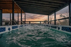 Ein Whirlpool mit Blick auf den Sonnenuntergang, eine Holzterrasse und ein Metallgeländer.