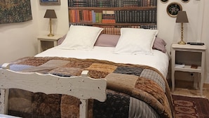 A bedroom with a large bookshelf, a bed with a quilt, a nightstand, and a table with a floral tablecloth. - An 18th-century tower in the heart of the Haut-Beaujolais region (Deux-Grosnes)