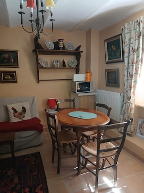 A dining area with a round wooden table, chairs, a red lamp, a microwave, and decorative plates on shelves.