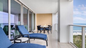 Een balkon met een tafel en stoelen, uitzicht op het strand, en een glazen deur die naar een andere kamer leidt.