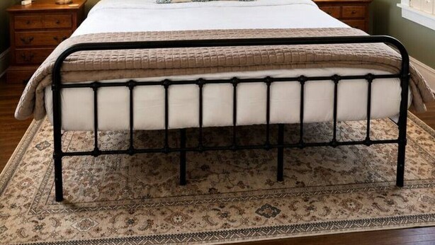 Ein Schlafzimmer mit einem Bett, Nachttischen, einem gemusterten Teppich und einem Fenster mit Fensterläden.