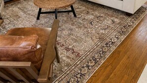 Ein Wohnzimmer mit einer Couch, einem Fernseher, einem gewobenen Couchtisch und einem gemusterten Teppich.