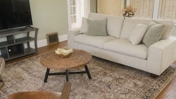 Een woonkamer met een bank, een televisie, een salontafel, een kamerkleed met dessin en een bruine leren fauteuil.