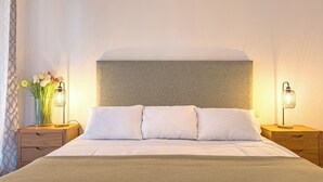 Un llit ben fet amb llençols blancs, dues taules de nit amb làmpades, i un ram de flors sobre una d'elles.