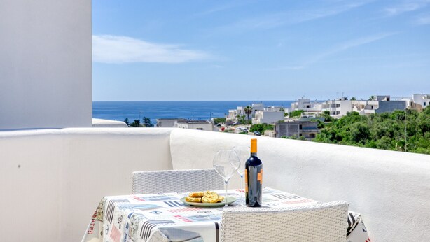 Una mesa con una botella y una copa en un balcón con vistas a un pueblo costero.
