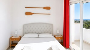 Una habitación de hotel con una cama, dos mesitas de noche, un ventanal con cortina roja y dos palas de madera en la pared.