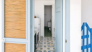 Un pasillo con piso estampado, una puerta con marco azul y un portón azul a la derecha.