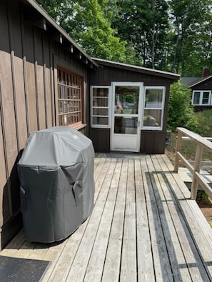 A wooden deck with a covered grill, a small building with a door, and a wooden railing. - Cozy Lakefront Cottage on Pleasant Lake's Lakeshore Drive (New London)