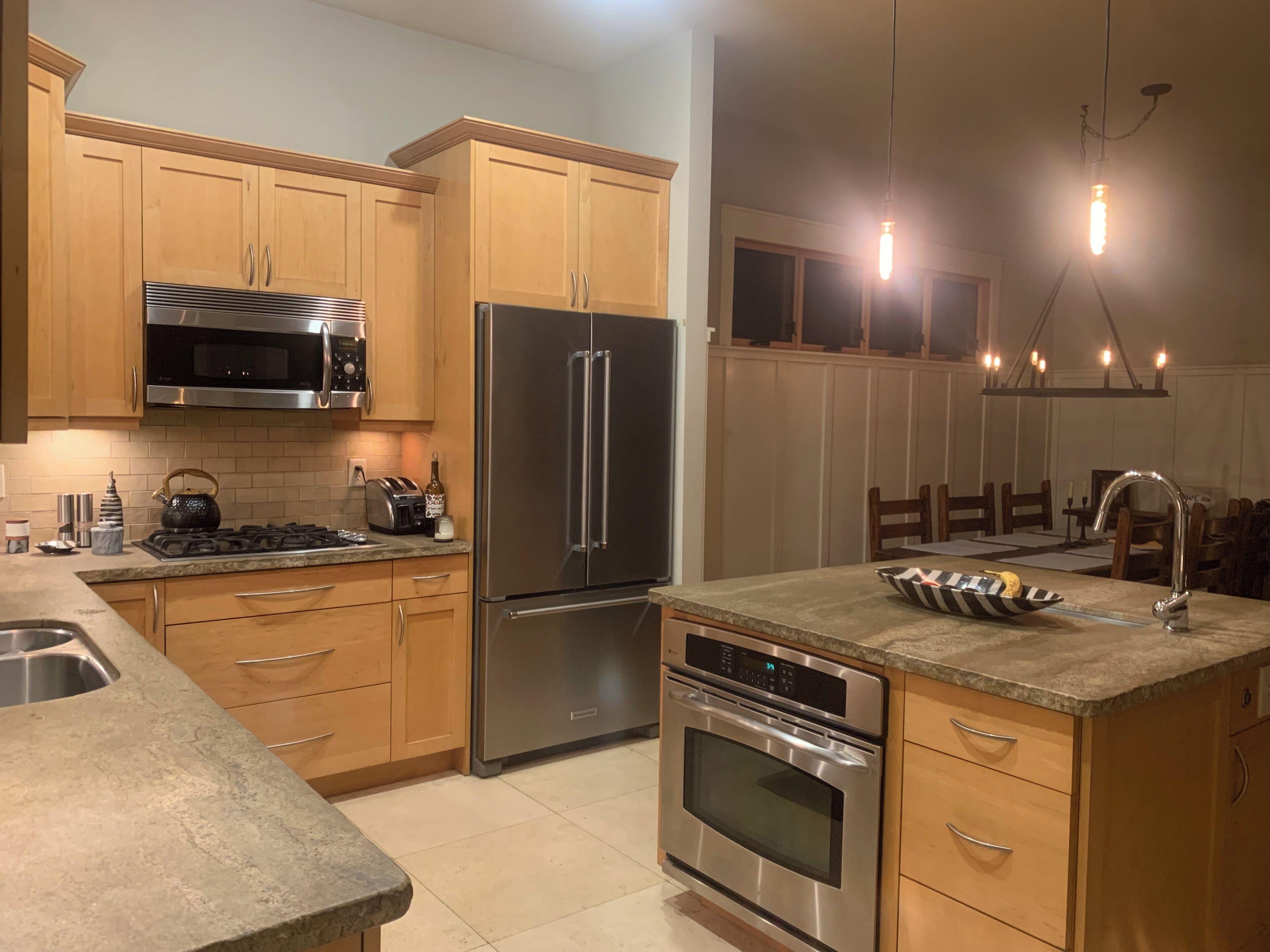A modern kitchen with stainless steel appliances, wooden cabinets, a granite countertop, and pendant lighting.