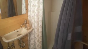 A wooden bathroom with a sink, mirror, shower curtain, and towel rack. - Cozy 1-bedroom cabin in amazing Winnie with AC (Winnie)