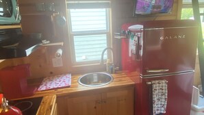 A compact kitchen with a sink, a red refrigerator, a microwave, and a television mounted on the wall. - Cozy 1-bedroom cabin in amazing Winnie with AC (Winnie)
