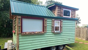 A small, green mobile home with a metal roof, a window with shutters, and a small deck area. - Cozy 1-bedroom cabin in amazing Winnie with AC (Winnie)