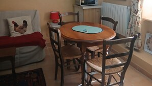 Ein Essbereich mit einem runden Holztisch, Stühlen, einer roten Lampe, einer Mikrowelle und dekorativen Tellern auf Regalen.