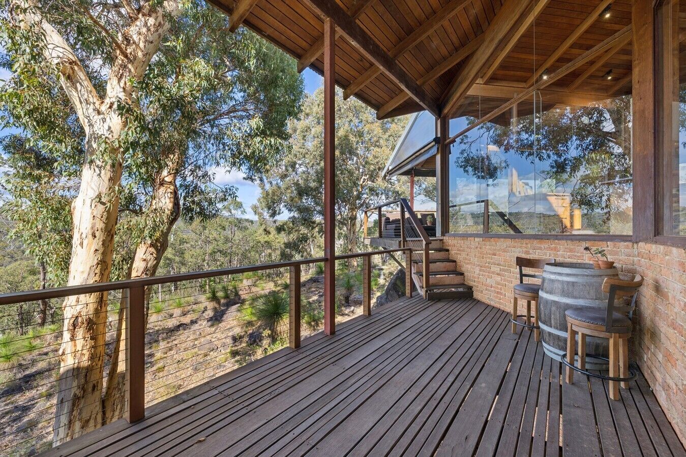 Une terrasse en bois dotée d’une balustrade en verre, d’un escalier et d’un espace détente avec un tonneau.
