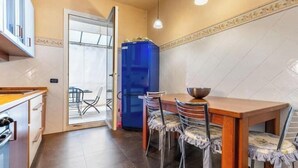 Una cocina con una mesa de comedor, sillas, un refrigerador azul y un ventanal de vidrio que da a un balcón.
