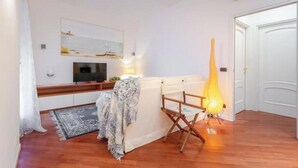 Una habitación con piso de madera, televisor, manta estampada, una silla de director y una escultura alta e iluminada.