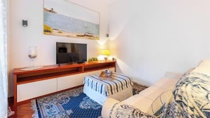 Una habitación de hotel con televisión, una mesita con lámpara, un sofá y una alfombra estampada.