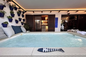 Un espace piscine aménagé avec des chaises longues, des plantes en pot et une vue sur l’intérieur.
