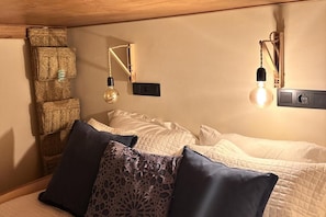 Een slaapkamer met een bed, kussens, een wandlamp en een stopcontact.