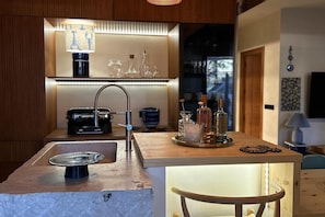 Een moderne keuken met een inbouweiland, een spoelbak en een bar voorzien van flessen en glazen.