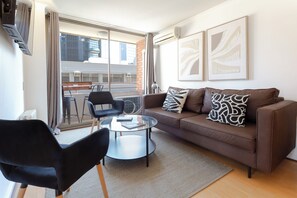 Ein Wohnzimmer mit braunem Sofa, schwarzen Sesseln, einem Glastisch und Kunstwerken an der Wand.