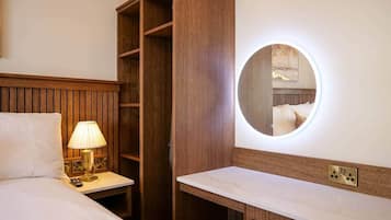 Une chambre d’hôtel comprenant un lit, une lampe de chevet, une armoire en bois et un miroir rond doté d’un éclairage intégré.