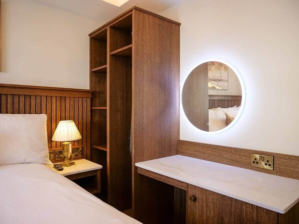 A hotel room with a bed, bedside lamp, wooden wardrobe, and a round mirror with built-in lighting. - Experience Dingle @ Main Street - Room 3 (Dingle)