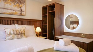 A hotel room with a bed, a wooden wardrobe, a round mirror, and a bedside table with a lamp. - Experience Dingle @ Main Street - Room 3 (Dingle)