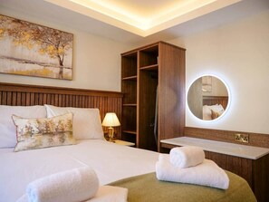 Une chambre d’hôtel avec un lit, une armoire en bois, un miroir rond et une table de chevet avec une lampe.