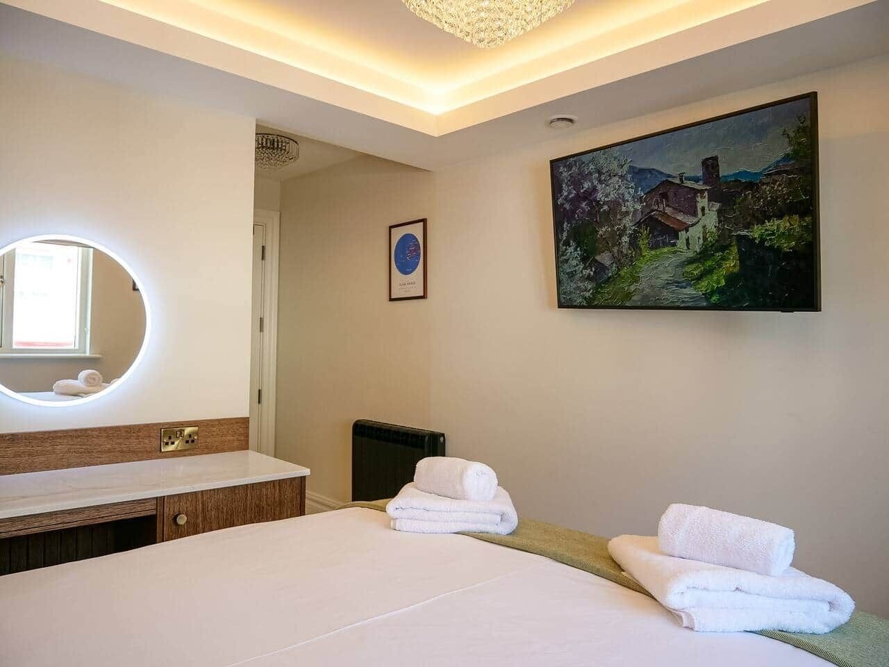 Ein Hotelzimmer mit einem großen Bett, einem runden Spiegel, einem Bild an der Wand und einem Fenster.