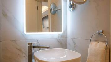 Une salle de bain avec un grand lavabo ovale, un miroir fixé au mur et un porte-serviettes.