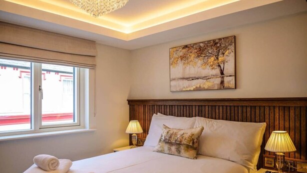 A hotel room with a large bed, two bedside lamps, a painting on the wall, and a window with a view. - Experience Dingle @ Main Street - Room 3 (Dingle)