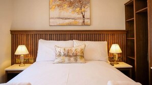A neatly made bed with a headboard, two bedside lamps, a painting above the bed, and a wooden wardrobe to the right. - Experience Dingle @ Main Street - Room 3 (Dingle)