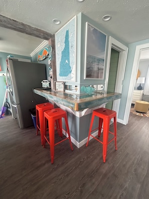 A kitchen with a bar area, red bar stools, a refrigerator, and a map on the wall.