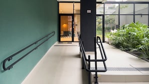 A modern building entrance with a green wall, a black pillar, and a glass door leading inside. - Today Butanã (São Paulo)