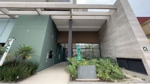 A modern building entrance with a green facade, a sign indicating 'TO DAY 1129', and a covered area with a wooden slatted roof. - Today Butanã (São Paulo)