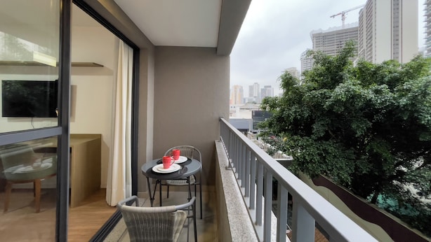 A balcony with a table and chairs, a potted plant, and a view of city buildings. - Today Butanã (São Paulo)