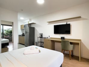 Habitación de hotel moderna con cama, escritorio, televisor, zona de cocina y balcón.
