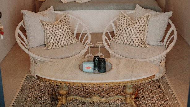 A bedroom with two white wicker chairs, a small round table, and a bed with multiple pillows. - Bleu guesthouse (Saint-François)